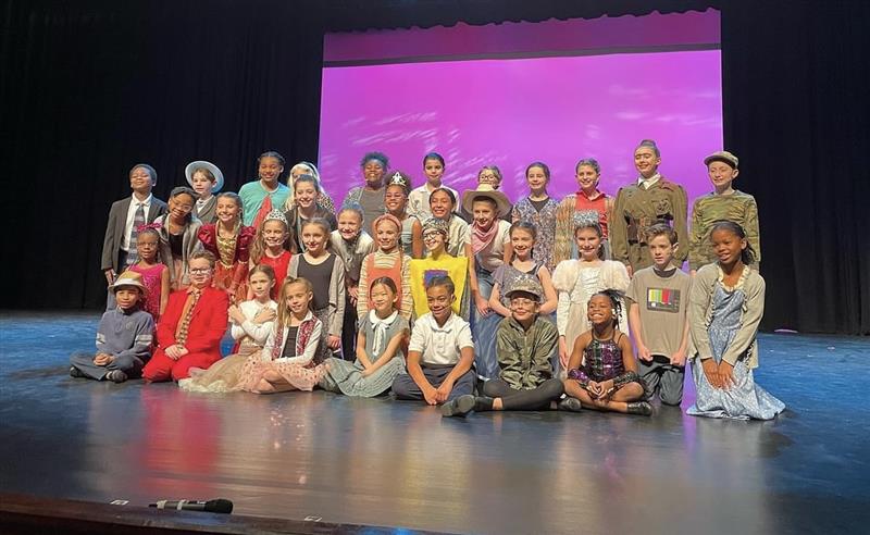 A group of students are gathered on stage in costume for Matilda Jr., smiling